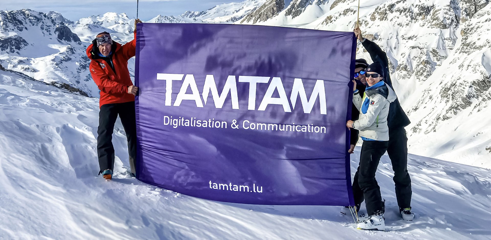 3 personnes tiennent le drapeau de TAM TAM au sommet de la montage 