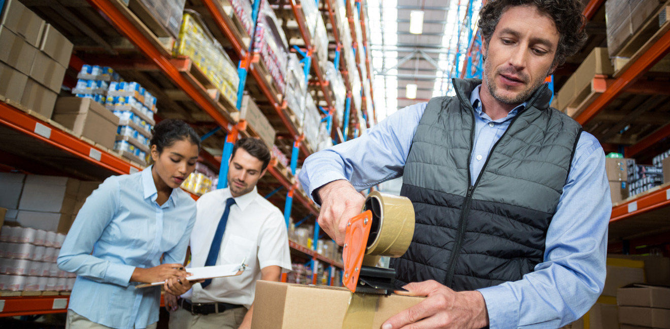Manutentionnaire qui ferme un carton dans un entrepôt